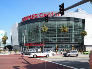 Staples Center - Jobs to Move America Exterior of Staples Center with glass curved facade, red Staples Center sign, palm trees, and street traffic nearby, including taxis and cars.